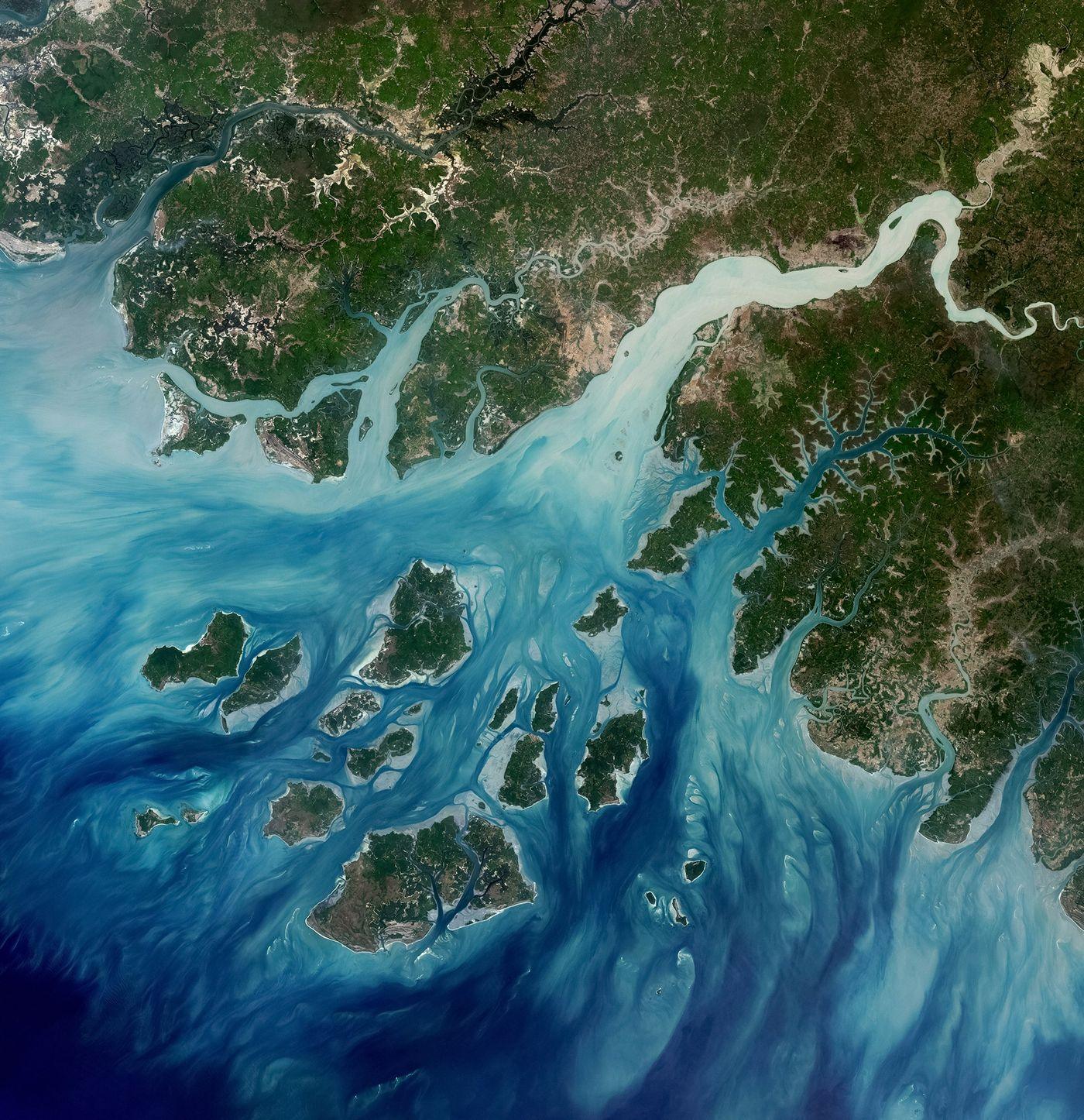 Satellite image of a river delta meeting the sea, with islands and channels in turquoise water